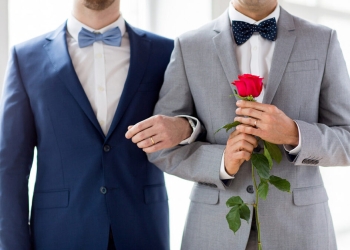 people, homosexuality, same-sex marriage and love concept - close up of happy male gay couple with red rose flower holding hands on wedding