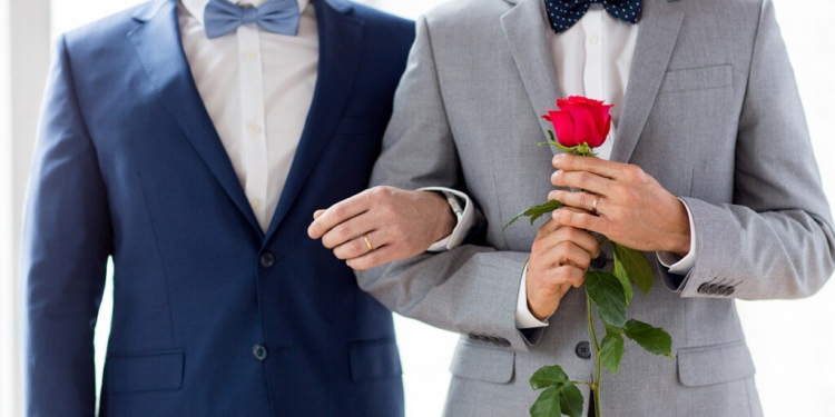 people, homosexuality, same-sex marriage and love concept - close up of happy male gay couple with red rose flower holding hands on wedding